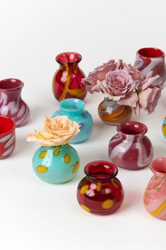 many different colored vases with flowers in them on a white surface, including one pink rose