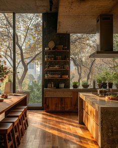 an open kitchen and dining room area with wooden flooring, large windows overlooking the trees