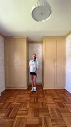 a woman is standing in the middle of a room with wooden floors and beige cabinets