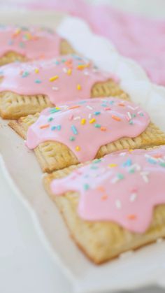 pink frosted donuts with sprinkles are on a white platter