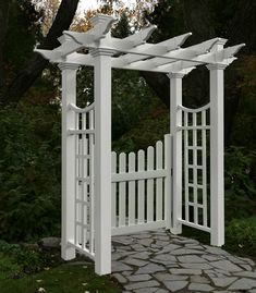 a white wooden arbor with stone walkway and trees in the background