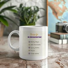 a white coffee mug sitting on top of a table next to a plant and books