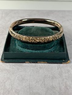 Great vintage hinged bangle bracelet. I believe this is made by Thomae & Sons Inc - there is a small lion figure etched into the clasp.  Appears to be gold filled but it is not marked as such.    7  inches around.  1/4 inch wide.  Good vintage condition - normal surface wear to the high points. There is some deep wear at the hinge - see the last photo.  Button easily works to open and close.  Front half has a scroll work design and the back half is plain. Vintage Jewlery, Scroll Work, Bracelet I, Work Design, Vintage Victorian, Hinged Bangle, Bangle Bracelet, Etching, Hinges