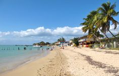 people are walking on the beach near some water and palm trees in front of houses