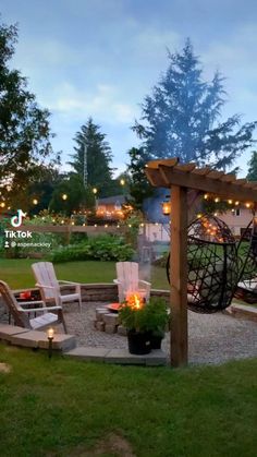 an outdoor fire pit surrounded by lawn chairs and lights in the evening light up the landscape