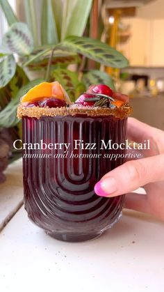 a hand holding a cup filled with fruit and topped with a cracker on top