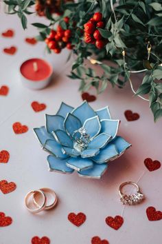 two wedding rings are sitting on a table next to a flower and some candles in the shape of hearts