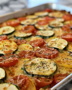 a casserole dish with tomatoes, zucchini and squash