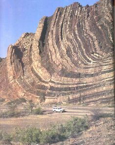 a truck is parked in front of a large rock formation on the side of a hill