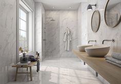 a bathroom with two sinks and mirrors on the wall, along with a bench in front of it