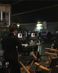 a woman is standing in front of several televisions with faces on them and behind her are chairs