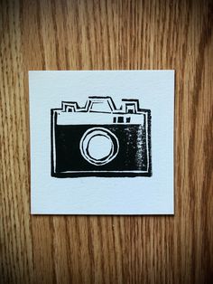 a black and white drawing of a camera on a piece of paper next to a wooden table