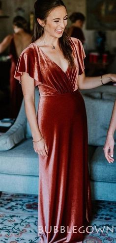 a woman in a red dress is smiling and standing near a couch with her hands on her hips