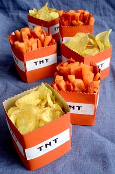 four orange boxes filled with chips and veggies on top of a blue cloth