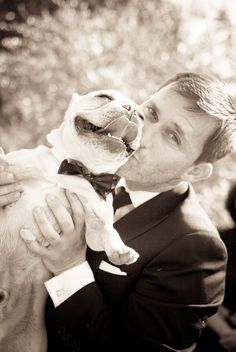 a man in a tuxedo holding a small dog up to his face while wearing a bow tie