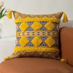 a yellow pillow with tassels on it sitting on a chair next to a vase