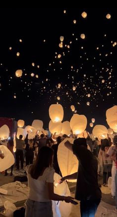 many people are releasing lanterns into the sky at night with their hands in each other's pockets