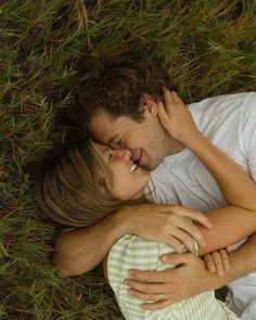 a man and woman laying in the grass hugging each other with their arms around one another