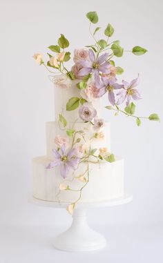 a white cake with purple flowers on top and green leaves on the side, in front of a white background