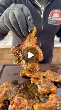 a man in black jacket and gloves holding up meat on top of a pan with sauce