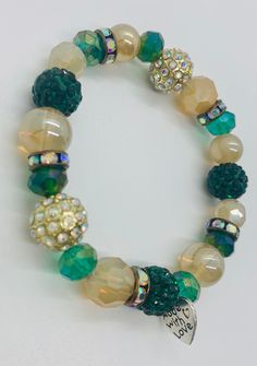 "The highlight of this handmade beaded stretch bracelet is the emerald and gold sparkle ball beads. These colourful crystallized beads complement the iridescent crystal spacer beads in antique gold throughout the bracelet. The rest of the bracelet is made up of green and gold beads in a variety of shapes, sizes and iridescent sheens. As the bracelet moves with wear the beads catch the light, emphasizing the unique sparkle and shimmer of the piece.  Each piece of jewelry from my store features the signature \"made with love\" heart charm. Includes a white organza bag to store." Gold Crystal Bracelets With Colorful Beads, Green Beaded Bracelet With Gold Beads, Green Crystal Bracelet With Colorful Beads, Green Crystal Round Beads Bracelets, Green Crystal Beaded Bracelets With Round Beads, Green Stretch Bracelet With Faceted Round Beads, Green Stretch Bracelet With Polished Round Beads, Green Stretch Bracelet With Polished Beads, Green Crystal Beaded Bracelets