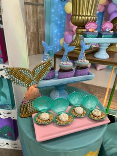 there are many cupcakes on the table with mermaid decorations around it and under them