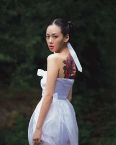 a young woman in a white dress with flowers on her back and shoulder, looking off to the side