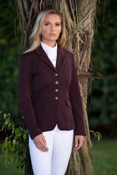 a woman standing in front of a tree wearing a horse riding jacket and white pants