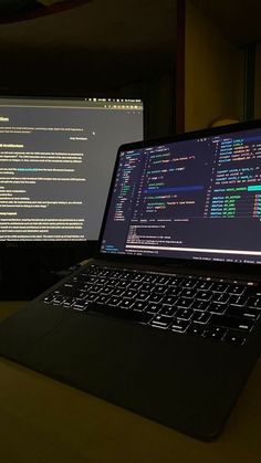 an open laptop computer sitting on top of a wooden desk next to two monitors with screens behind it