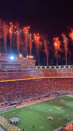 fireworks light up the night sky over an orange and white football stadium as spectators watch