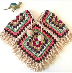 a crocheted bag with tassels and a toy dinosaur on the side