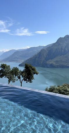 an outdoor swimming pool with mountains in the background and blue water on both sides, surrounded by greenery