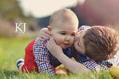 a couple of kids laying on top of each other in the grass with their faces close to each other