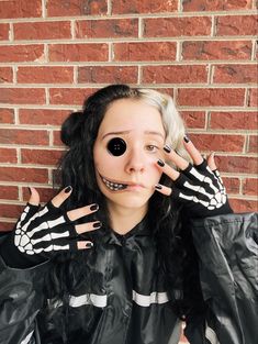 a woman with fake hands and skeleton makeup on her face, wearing black gloves while standing in front of a brick wall