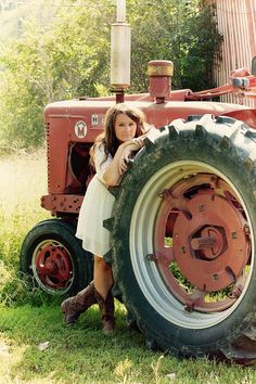 a woman standing next to an old red tractor