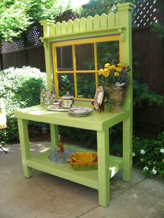 a green bench with a yellow window and flowers in the potted planter next to it