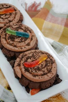 three chocolate cookies with gummy bears on top are in a white plate and one cookie has been cut into the shape of a spiral