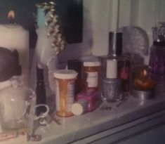 various items are sitting on a shelf in front of a window with candles and bottles