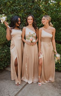 three bridesmaids pose for a photo in front of some bushes and greenery