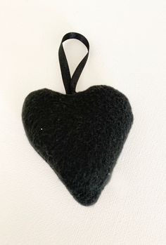 a black heart ornament hanging on a white surface with a black ribbon around it