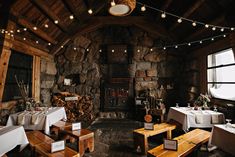 a restaurant with tables and benches in front of a fire place that has lights strung from the ceiling