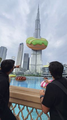 two people looking at doughnuts in front of a cityscape with skyscrapers