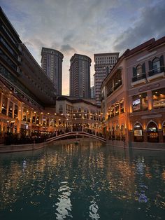 the city is lit up at night with buildings in the background and water running through it