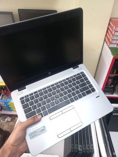 a person holding up a laptop computer in front of a shelf with other items on it