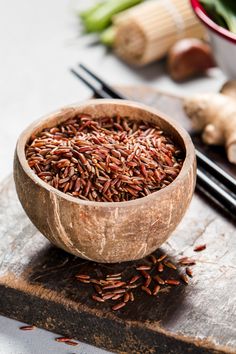 a wooden bowl filled with brown rice next to chopsticks