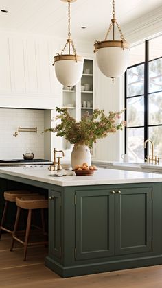 a kitchen with green cabinets and marble counter tops, two pendant lights over the island