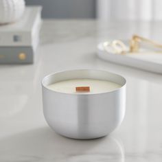 a white candle sitting in a silver bowl on top of a counter next to a book