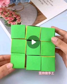 someone is holding a green cube with four squares in it and the video below shows how to make an origami cube