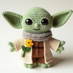 a crocheted yoda doll with a flower in it's hand, on a white background