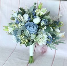 a bridal bouquet with blue flowers and greenery on a white clothed chair